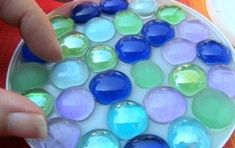 someone is pointing at some colorful glass balls on a plate