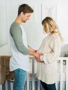 a man and woman standing in front of a crib holding their hands on the belly