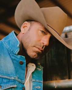 a man wearing a cowboy hat leaning against a wooden fence with his hand on his head