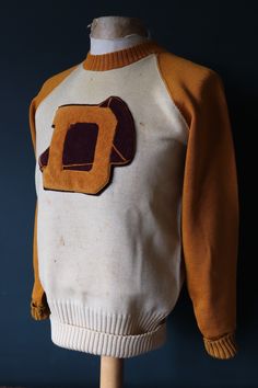 "An American cream and gold wool varsity sweater, dating from the late 1940s or early 1950s. Noted flaws - discolouration and marking throughout, holes at the collar, long rib area, back of the shoulders and cuffs - please see photos. Excellent condition otherwise, thinner 100% worsted wool, round collar with 1/4 zip at the back, long rib waistband, zip runs smoothly, large D cheerleader patch on the centre front, roll back cuffs, great style. Measurements taken lying flat -  Pit to pit - 19.5\" Vintage Mustard Sweater For Winter, Retro Cotton Beige Sweater, Retro Beige Cotton Sweater, Vintage White Sweater For College, Retro Brown Cotton Sweatshirt, Retro Sweater For College In Fall, White Vintage Sweater For College, Vintage Mustard Sweater For Fall, Mustard Retro Long Sleeve Sweater