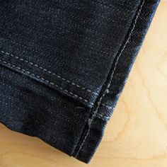 the back pocket of a pair of dark blue jeans on a wooden surface with white stitching