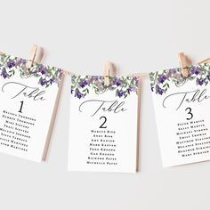 purple flowers and greenery are hanging from clothes pins to display the seating cards for an outdoor wedding