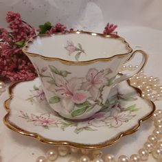 an antique tea cup and saucer with flowers on it, surrounded by pearl necklaces