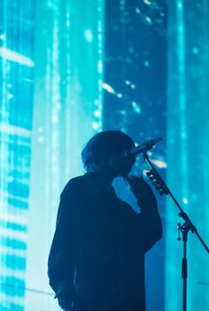 a man standing in front of a microphone on top of a stage with lights behind him