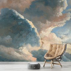 a chair sitting in front of a wall with clouds painted on it and a round ottoman next to it