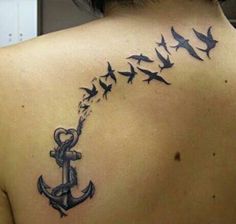 the back of a woman's shoulder with an anchor and birds tattoo on it