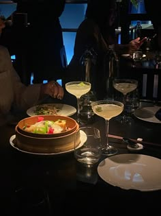 a woman sitting at a table in front of wine glasses with food and drinks on it