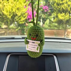 a green crocheted stuffed animal hanging from the dashboard of a car with a sticker on it