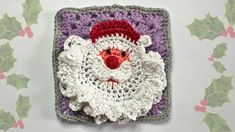 a crocheted square with a santa claus face on it and holly leaves in the background