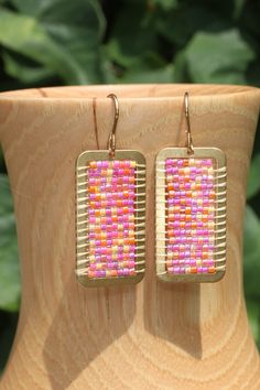 a pair of pink and orange beaded earrings sitting on top of a wooden vase