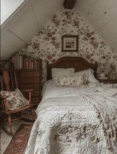 a bed sitting under a slanted ceiling next to a chair and table in a bedroom