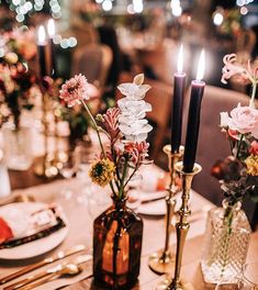 the table is set with candles and flowers in vases, plates and silverware