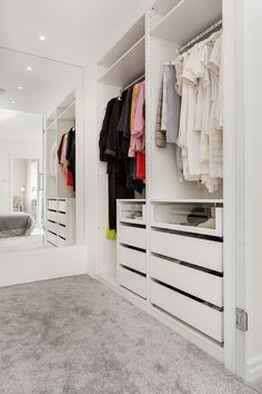 a white closet with drawers and clothes hanging on the wall next to a large mirror