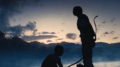 two men are standing in the water with their surfboards and one is holding an oar