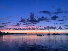 several sailboats are floating in the water at sunset or dawn with clouds and blue sky