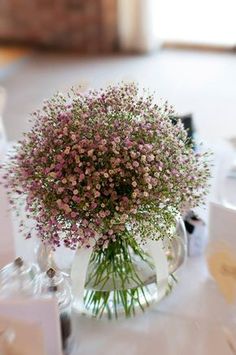 a vase filled with pink flowers sitting on top of a white tablecloth covered table