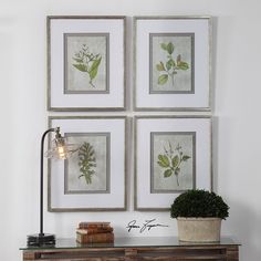 four framed pictures hang on the wall above a table with a lamp and books in front of it