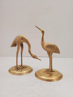 two gold colored metal birds standing next to each other on top of a white surface