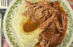 a white plate topped with meat and mashed potatoes covered in gravy next to a fork