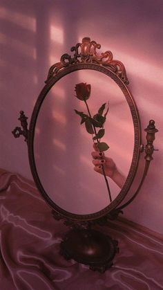 a person's hand holding a rose in front of a round mirror on a bed