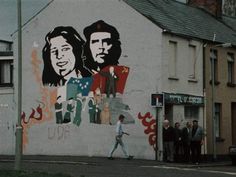 a group of people standing in front of a building with graffiti on the side of it