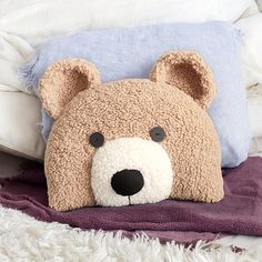 a teddy bear pillow sitting on top of a bed next to a purple and white blanket