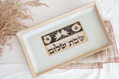 "This beautiful bread plate is made of ceramic stoneware.  In the center of the tray there is drawing of a couple of birds (symbol of love and joy) and on the side pomegranates (symbol of abundance and prosperity). The typography (\"Shabbat Shalom\") is made according to the traditional biblical Hebrew writing.  These Shabbat Shalom plate could be user for Challah, candle sticks or Kiddush cup.  It is the perfect way to celebrate the Shabbat. Made on the slab by free hand, fired at 2228oF/1220oC which ensure durability and strength. Made of non-toxic materials (lead free) and perfectly safe to eat of. Oven microwave and dishwasher proof.  L tray Size: Plate length  11.8\" (30cm). Plate width  6.6\" (17cm). Please allow for small differences in size and shape, as they are all hand made. All Drawing Of A Couple, Hebrew Writing, Beautiful Bread, Biblical Hebrew, Kiddush Cup, Ceramic Stoneware, Shabbat Shalom, Candle Sticks, Jewish Gifts