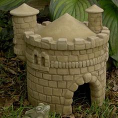 a statue of a castle made out of clay sitting on the ground in front of some plants