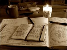 an open book sitting on top of a wooden table next to a cup and pen