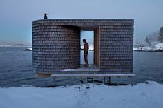 a woman standing in the doorway of a building on top of snow covered ground next to water