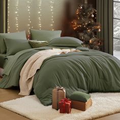 a bed with green comforter and pillows next to a christmas tree