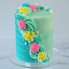 a green cake with blue icing and flowers on the top is sitting on a clear plate