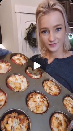 a woman holding up a tray of mini pizzas