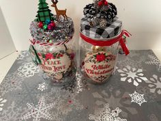 two jars filled with christmas decorations on top of a snowflake covered tablecloth