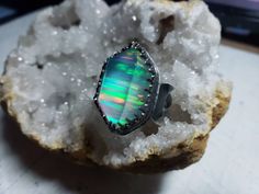 "This listing is for one handmade ring. The aura opal is a synthetic opal made of the same components as natural opal. This aura opal has been topped with quartz. This stone has a soft blue hue with stripes of rainbow flashes. The stone is set in a raised crown-like setting. The band is a doubled patterned band with a crescent moon on ether side. The ring is made with .925 sterling silver. Ring size: 8.75 (will fit a 8.25-8.5) Height x width: 1 x 7/8\" (in inches) The doubled band has a more snu Iridescent Opal Ring As A Gift, Iridescent Opal Ring Gift, Iridescent Opal Ring With Gemstone, Iridescent Opal Ring Perfect For Gifts, Spiritual Opal Ring For Healing, Unique Handmade Iridescent Opal Ring, Unique Green Opal Ring, Unique Iridescent Crystal Ring With Gemstone, Unique Iridescent Moonstone Ring For Gift