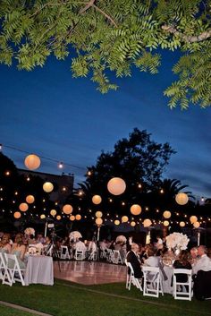 an outdoor wedding reception with paper lanterns hanging from the trees