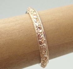 a close up view of a bracelet on a woman's arm with flowers and leaves engraved on it