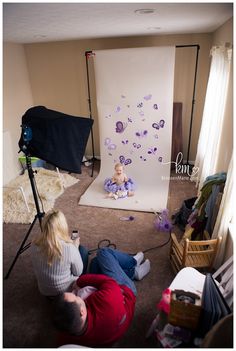 two people sitting on the floor in front of a white backdrop with purple butterfly decorations