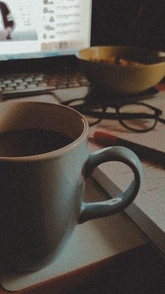 a cup of coffee sitting on top of a desk next to a computer monitor and keyboard