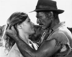 the man and woman are embracing each other in black and white photo, one is wearing a cowboy hat