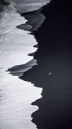 a person walking on the beach with their surfboard in hand and water coming up from the shore