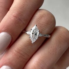 a woman's hand holding an engagement ring with a diamond in the middle and two diamonds on each side