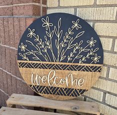 a welcome sign on the side of a brick building with flowers and leaves painted on it