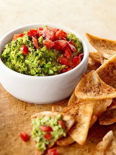 a white bowl filled with guacamole and chips on top of a wooden cutting board