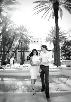 a man and woman standing next to each other in front of palm trees on a sunny day