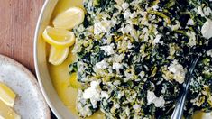 a white plate topped with greens and feta cheese next to two lemon wedges