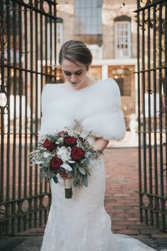 a woman in a wedding dress holding a bouquet and fur stoler over her shoulder