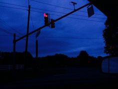 a traffic light hanging over a street next to power lines and trees at night with blue sky in the background