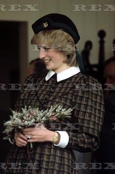 a woman wearing a hat and dress holding flowers in her hands while standing next to other people