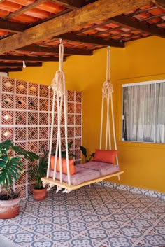 a hammock chair hanging from the ceiling in front of a yellow wall and potted plant